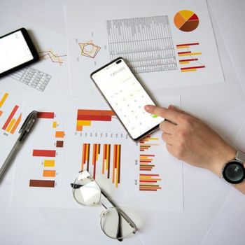 Er liggen 2 smartphone's op een tafel met papieren waarop grafieken en cijfers staan.